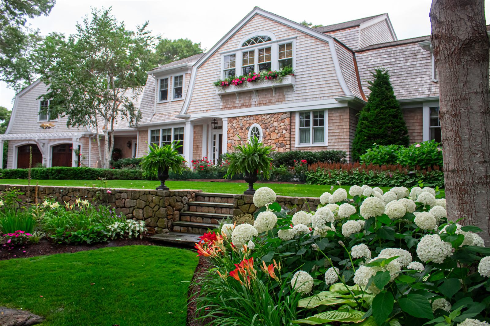 Estate home with layered garden beds and a stone retaining wall